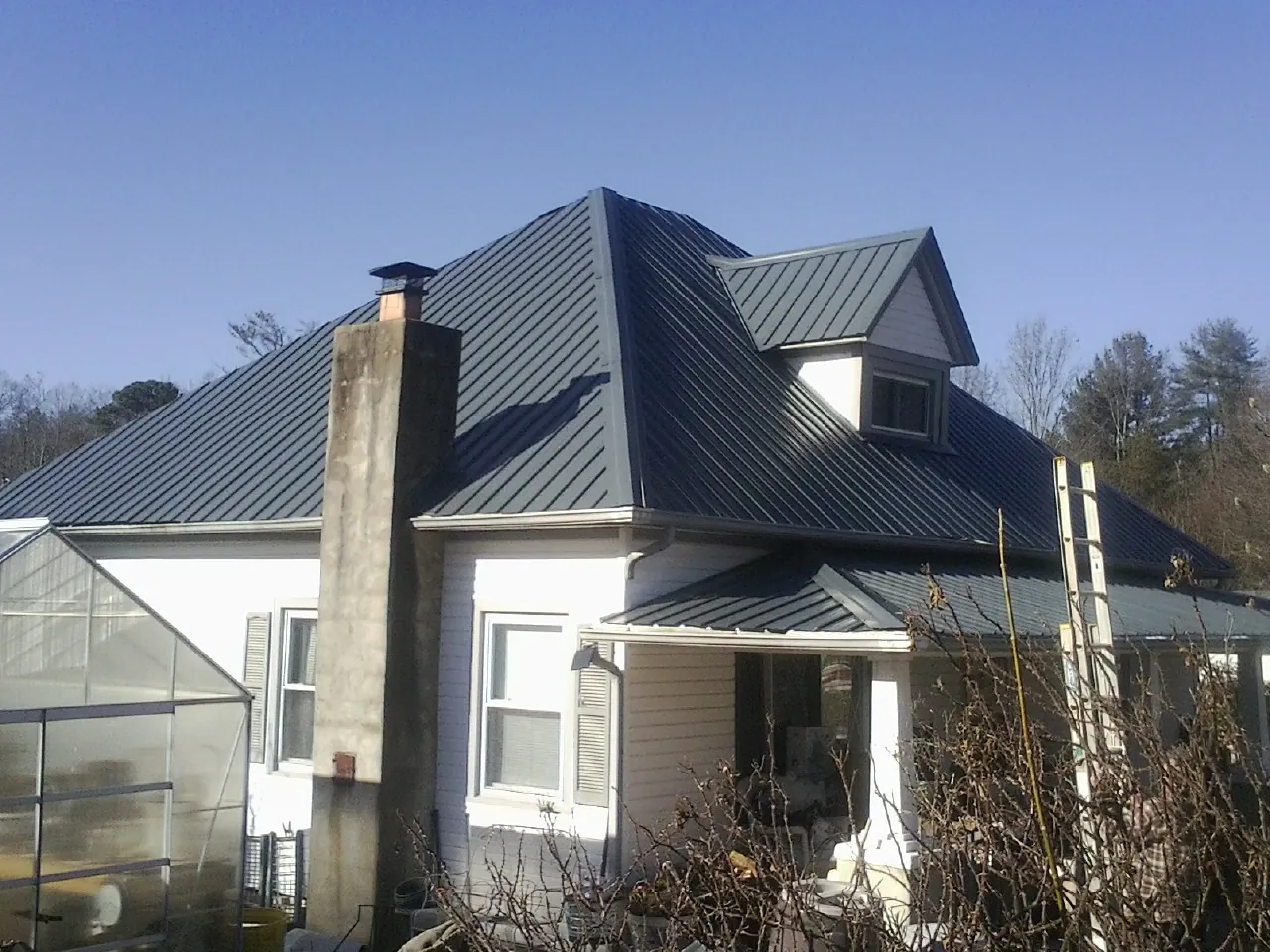 Dark blue standing seam metal roof on a white farmhouse with dormer — Slate & Tile Roof Repair by Roofing Brothers in Greenfield