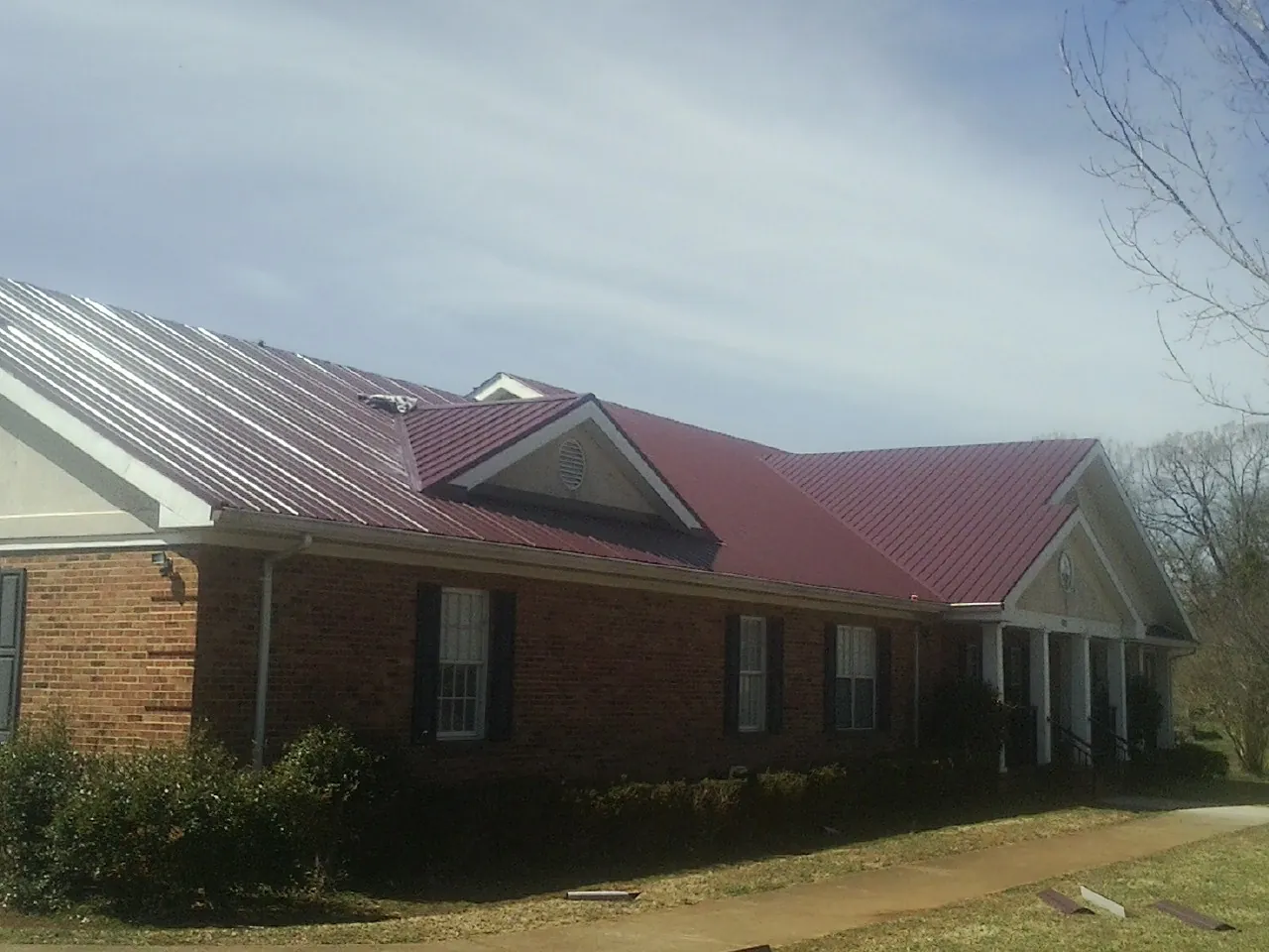 Red metal roof with gabled entries on a long brick building, from a Hail Damage Roof Repair job in Greenfield