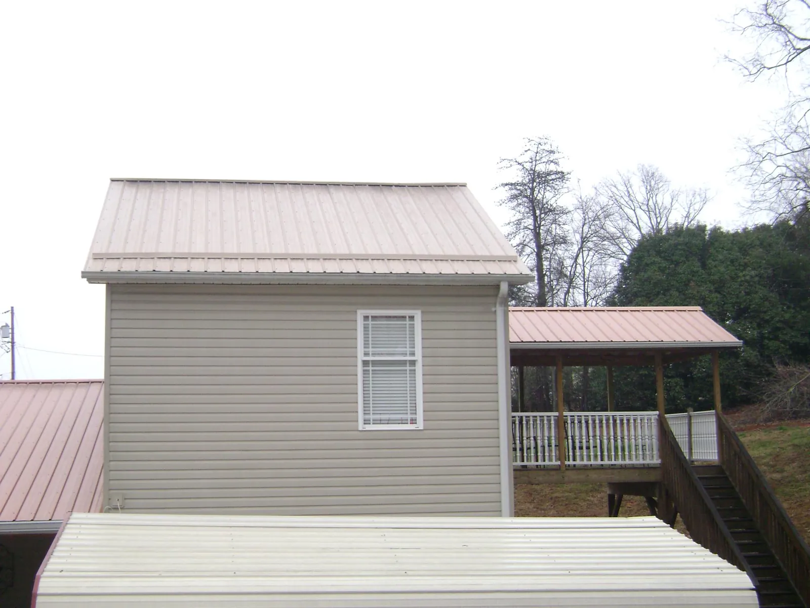 Tan metal roofs on a two story addition and attached porch, from a Roof Replacement job in Greenfield